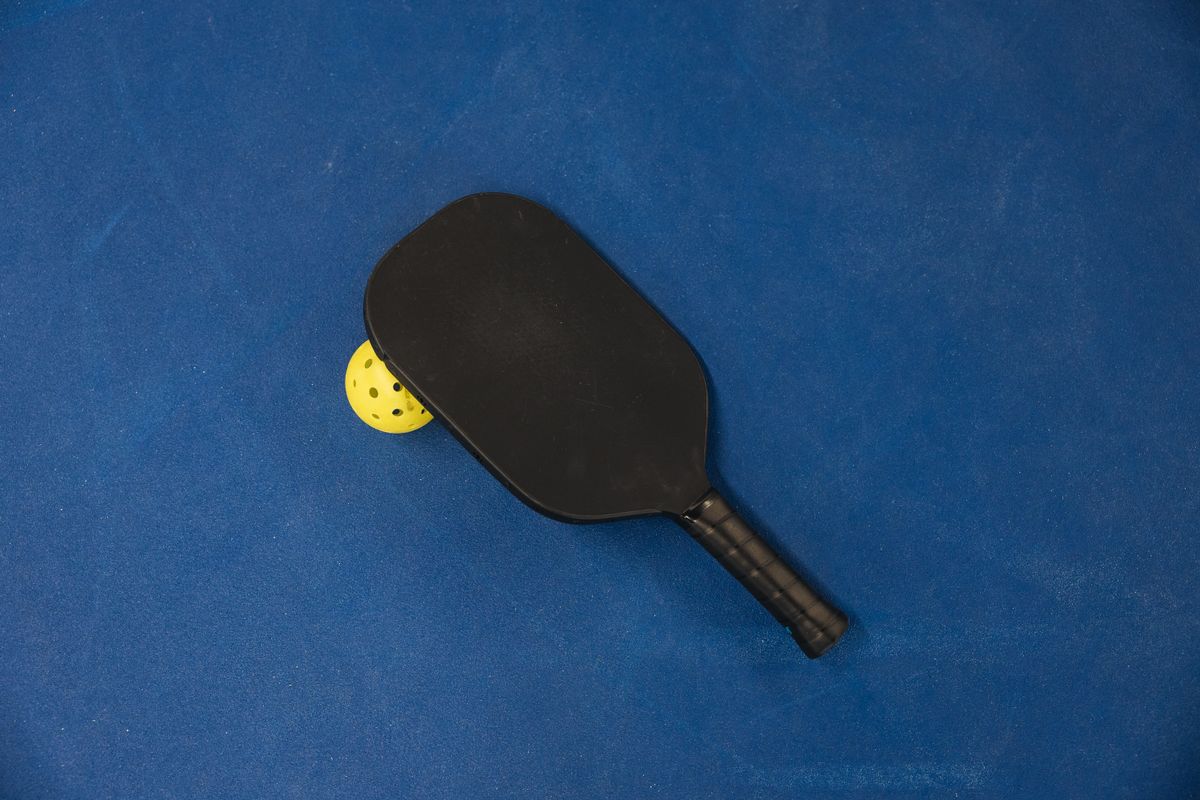 Pala de pickleball con pelota junto al grip sobre pista azul