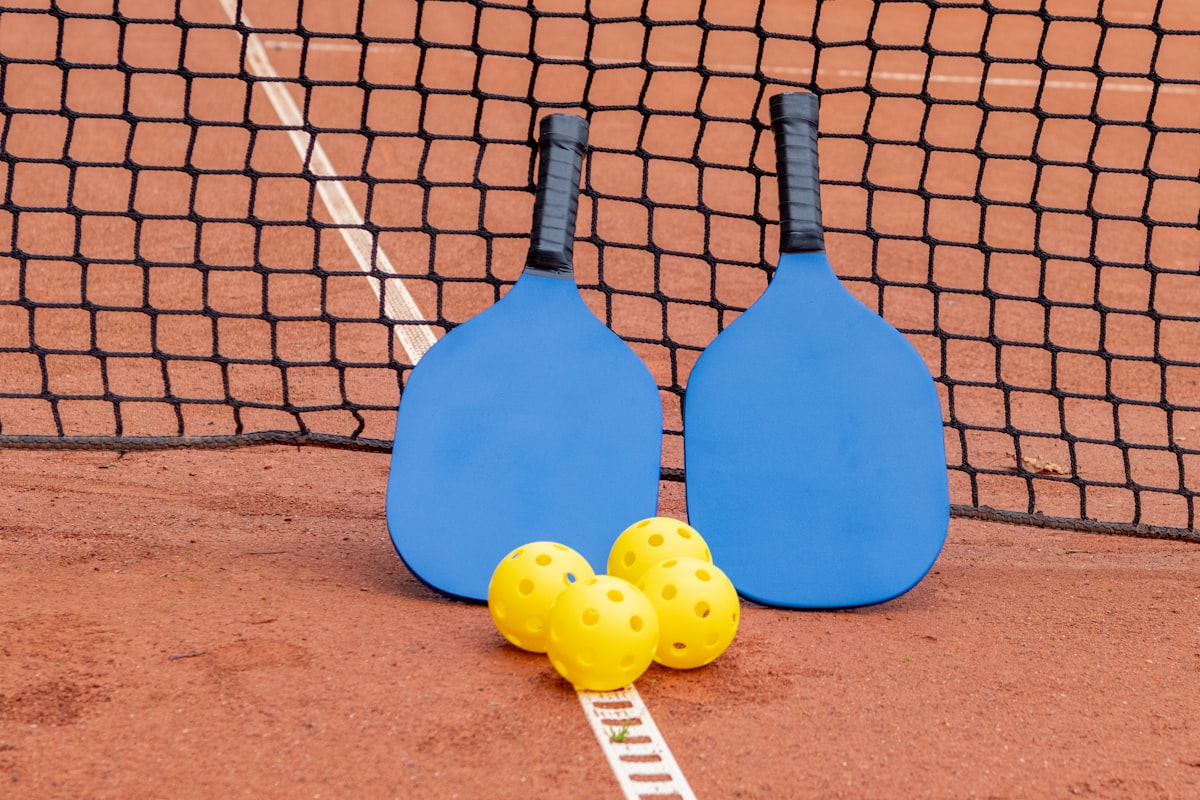 Dos palas de pickleball azules y pelotas amarillas junto a la red